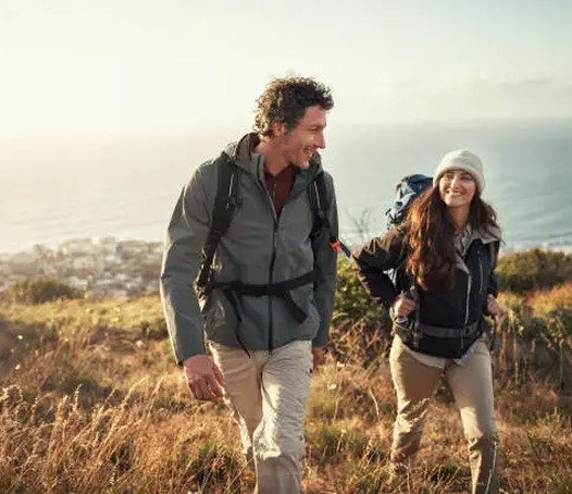 Two hikers smiling on a coastal trail at sunrise