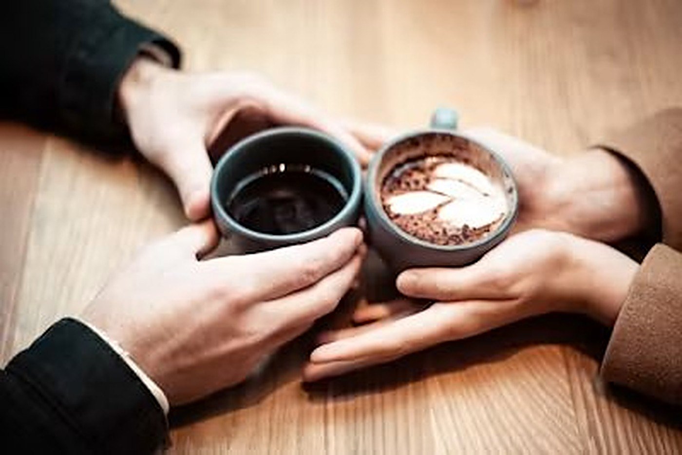 Two people holding hands across a cafรฉ table over two cups of coffee