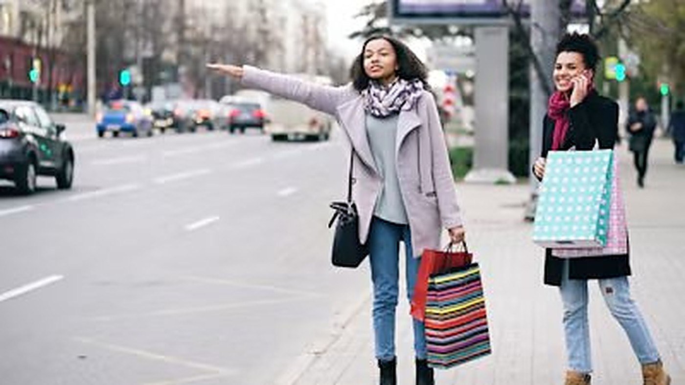 Two friends with shopping bags hailing a taxi in town