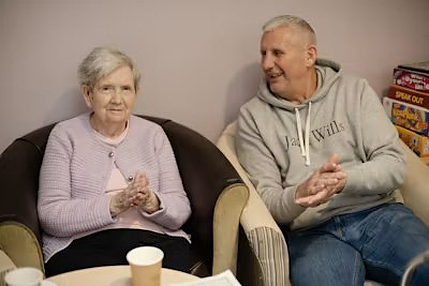 An older woman and a younger man clapping and smiling together