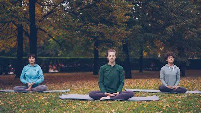 Three people meditating on yoga mats in an autumn park