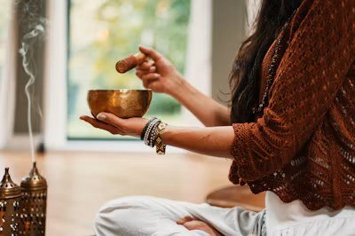 A woman playing a singing bowl beside incense during meditation