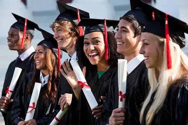 Smiling graduates in caps and gowns holding their diplomas