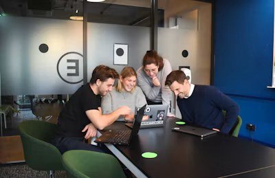 Four colleagues smiling around laptops at a meeting table